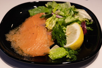 Trout with greens, salad and lemon on a black plate. Shallow depth of field
