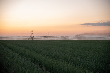 Fototapeta na wymiar Boom Irrigation of Field During Summer Sunset Dusk. Moody Feel.