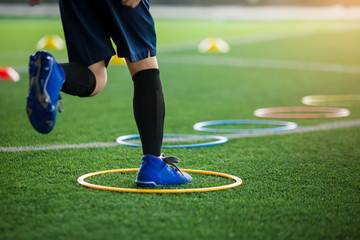 selective focus to kid soccer player Jogging and jump at ring ladder marker on green artificial...