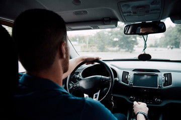 Driver man driving in car behind the wheel view from the back seat