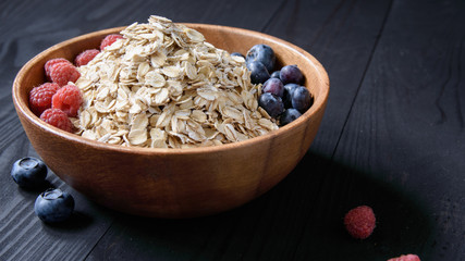oatmeal with blueberries and raspberries in a wooden bowl on a black wooden table