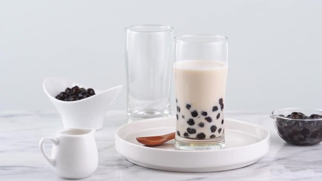 Tasty tapioca pearl bubble milk tea in glass, popular drink in taiwan on bright marble table and white tray, homemade concept. 4K Zoom in shot video