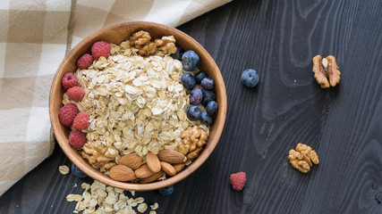 oatmeal with blueberries, raspberries, almond and walnuts in a wooden bowl on a black wooden table