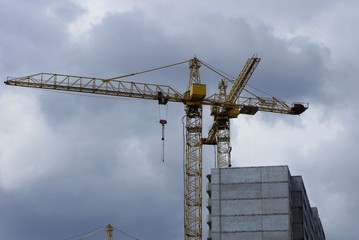 yellow iron tower crane over a gray unfinished house against the sky