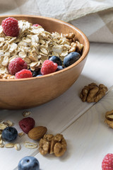 oatmeal with blueberries, raspberries, almond and walnuts in a wooden bowl on a black wooden table