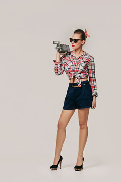 pin-up girl in plaid shirt and sunglasses holding old vintage camera.