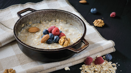 oatmeal with blueberries, raspberries, almond and walnuts in a metal bowl on a black wooden table