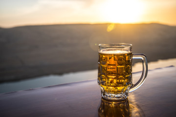 Glass of beer on a beach at sunset. Cooling summer drink concept. Close Up of A Glass of Draught Beer with the Bokeh of Sunlight Background