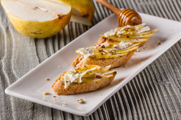 Appetizer bruschetta with pear, honey, walnut and blue cheese on white plate