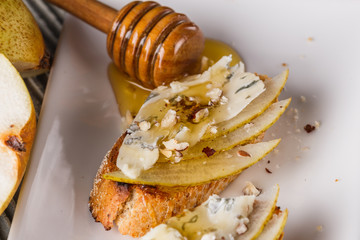Appetizer bruschetta with pear, honey, walnut and blue cheese on white plate