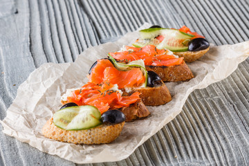 Bruschetta with smoked salmon, fresh cucumber, black olives and camembert on crumpled baking paper
