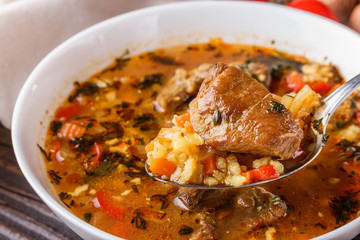 Georgian soup. Kharcho with rice, tomato, beef, garlic and herbs in bowl on wooden table