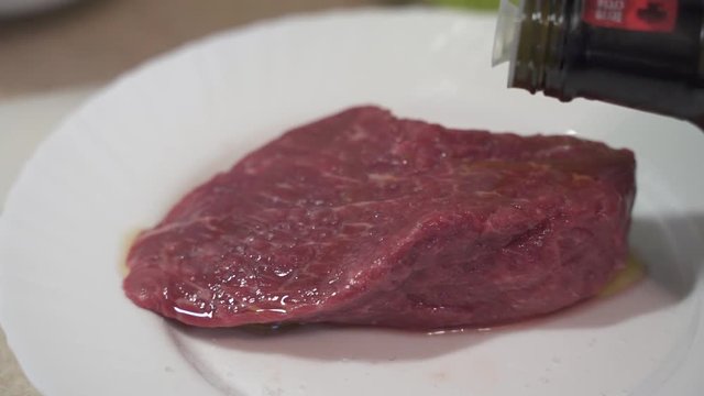 Raw rib eye beefsteak covered with organic olive oil by cooking brush to preserve the moisture inside a meat during pan frying