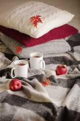 Obraz na płótnie Canvas Home comfort and warmth in the autumn time. Gray plaid, knitted pillows, tea and autumn red maple leaves.