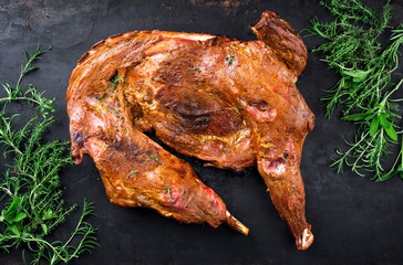 Barbecue half of dairy goat with shoulder and leg garnished with a bouquet garni as top view on an old rustic board