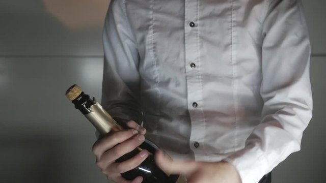 The waiter a man in a white shirt opens the bottle of champagne foam flows