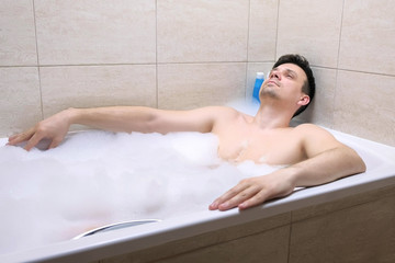 Obraz premium 30s man sitting in the bathroom, relaxing and falling asleep in the evening in foam after hard day.