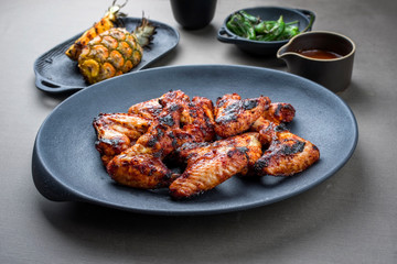 Exotically barbecue chicken wings with hot chili sauce, jalapeno and pineapple as closeup on a cast iron plate