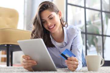 Happy natural brunette using credit card and laptop in the living room.
