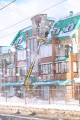 The cleaning service cleans the snow from the roof of the house. Workers on special equipment clean snow in winter. Cleaning the ice and snow from the roofs of houses.