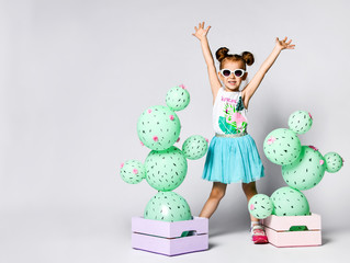 young blond girl raised her hands up from joy on the background on a fictional cactus in a wooden...