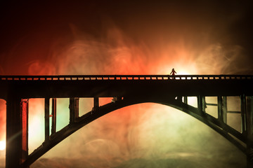 Artwork decoration. Silhouette of powerful metallic bridge at night with foggy backlight. Silhouette of person standing on bridge.