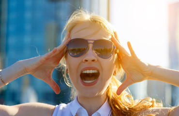 young blonde in sunglasses screams open rod and holds her head , bright sunlight and blurred...