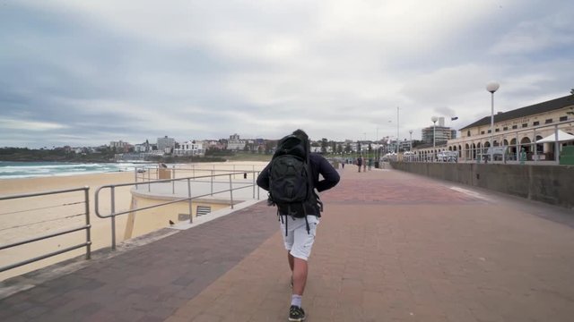 A male tourist with backpack walking along Bondi Pavilion overlooking the surf beach.