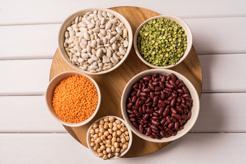 Top view of assortment of peas, lentils, beans and legumes over white wooden background.