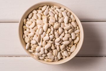 Top view white beans in a bowl over white wooden background.
