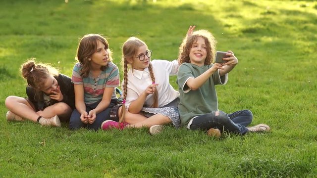 Classmates make selfie in the park. Four schoolchildren, teenagers are photographed on a smartphone. School friendship, happy school holidays