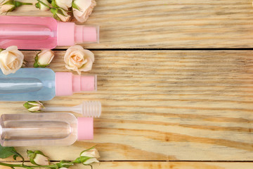 Face and body cosmetics in pink bottles with fresh roses on a natural wooden background. creams and lotion. spa. top view. space for your text