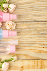 Face and body cosmetics in pink bottles with fresh roses on a natural wooden background. creams and lotion. spa. top view. space for your text