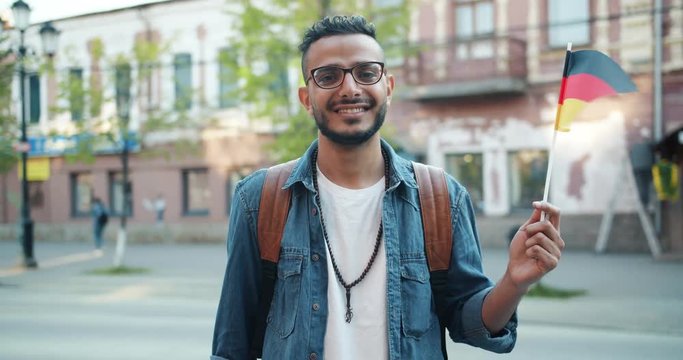 Slow motion of happy Middle Eastern tourist holding German flag outdoors smiling looking at camera. World countries, modern youth and immigration concept.