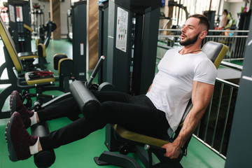 Fototapeta na wymiar Man trains legs in gym. Handsome bearded bodybuilder training