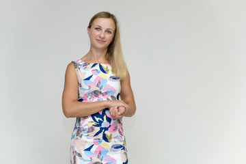 Portrait of a pretty beautiful adult female 35 years old blonde on a white background in a light dress with a pattern. Standing in front of the camera, smiling.