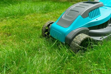  Lawn mower mowing green grass. Summer work in the garden.