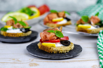 small canape with pink salmon fish, cucumber, tomato, olive and lemon on a light wooden background