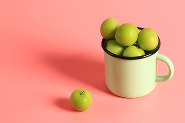 green cherry plum in an enamel mug on a pink background. Creative minimalist style. healthy food