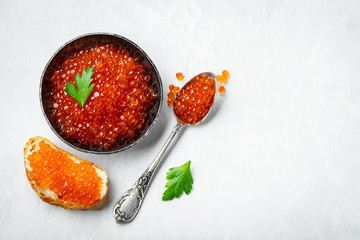 Delicious red caviar in black bowl on a light concrete background. Top view with copy space. Flat...