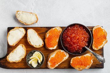 Close-up red caviar in bowl and Sandwiches on wooden cutting board on white background. Top view with copy space. Flat lay