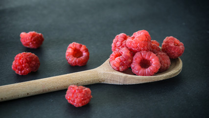 Fresh raspberries in a wooden spoon on black background