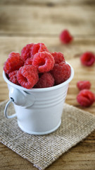 Close up of white bucket full of raspberry fruit on wooden table