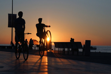 Obraz premium Two cyclists silhouettes on sea beach embankment sunset background