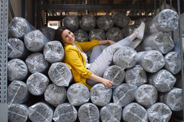 The girl sits on the rolls of the mattress in the warehouse. Wholesale and purchase. Self-service warehouse