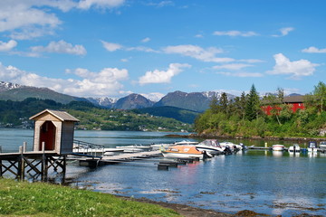 Fototapeta premium Norwegian landscape with Hardanger fjord, mountains, boats, pier , flowers and cloudy sky in Norway