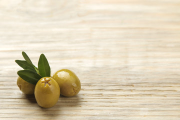 Green olives in a bowl with leaves on a natural wooden table. close-up. place for text.