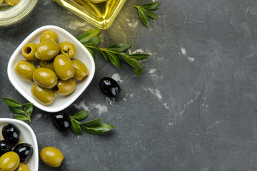 Green and black olives in a white ceramic bowl with leaves on a dark graphite background. top view. space for text