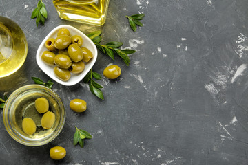 Green olives in a white ceramic bowl with leaves on a dark graphite background. top view. space for...