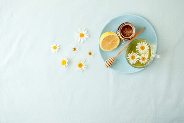 Chamomile flowers and chamomile tea. Chamomile tea in glass teacup with flowers, honey and lemon, top view, prevention of seasona flu colds